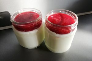 Deux pots de yaourt nature avec du coulis de framboises dessus